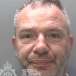 Police custody photograph of Dominik Szymanski, a 47-year-old man with short greying hair and stubble, wearing a grey T-shirt.