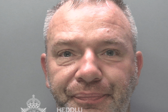 Police custody photograph of Dominik Szymanski, a 47-year-old man with short greying hair and stubble, wearing a grey T-shirt.