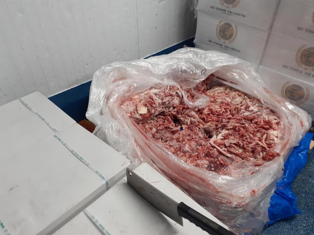 A meat processing factory floor with industrial mixing machines, trolleys of pink processed meat paste and colourful tubs of pale ingredients