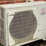 A Mitsubishi Electric air-source heat pump unit mounted against the brick wall of a house.