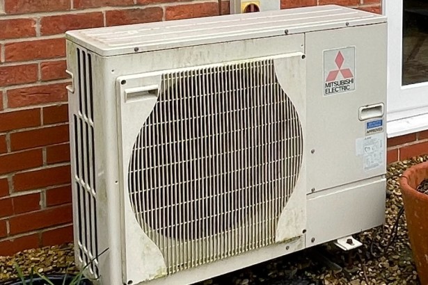 A Mitsubishi Electric air-source heat pump unit mounted against the brick wall of a house.