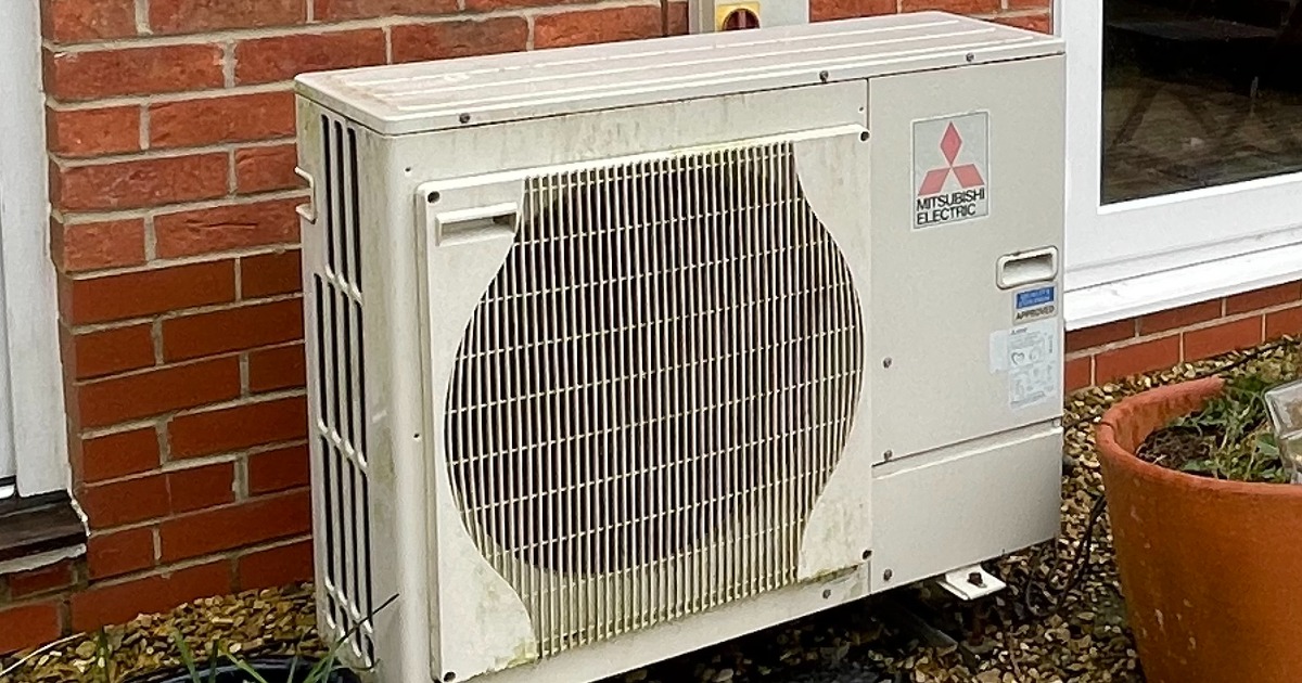 A Mitsubishi Electric air-source heat pump unit mounted against the brick wall of a house.
