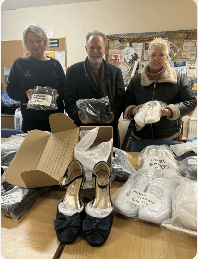 Three people stand behind a table of donated shoes and trainers in clear bags at the Links centre.