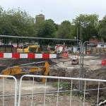 Excavation work in Castle Square behind site fencing, with a Thomas Plant Hire digger and the ruins of Swansea Castle behind.