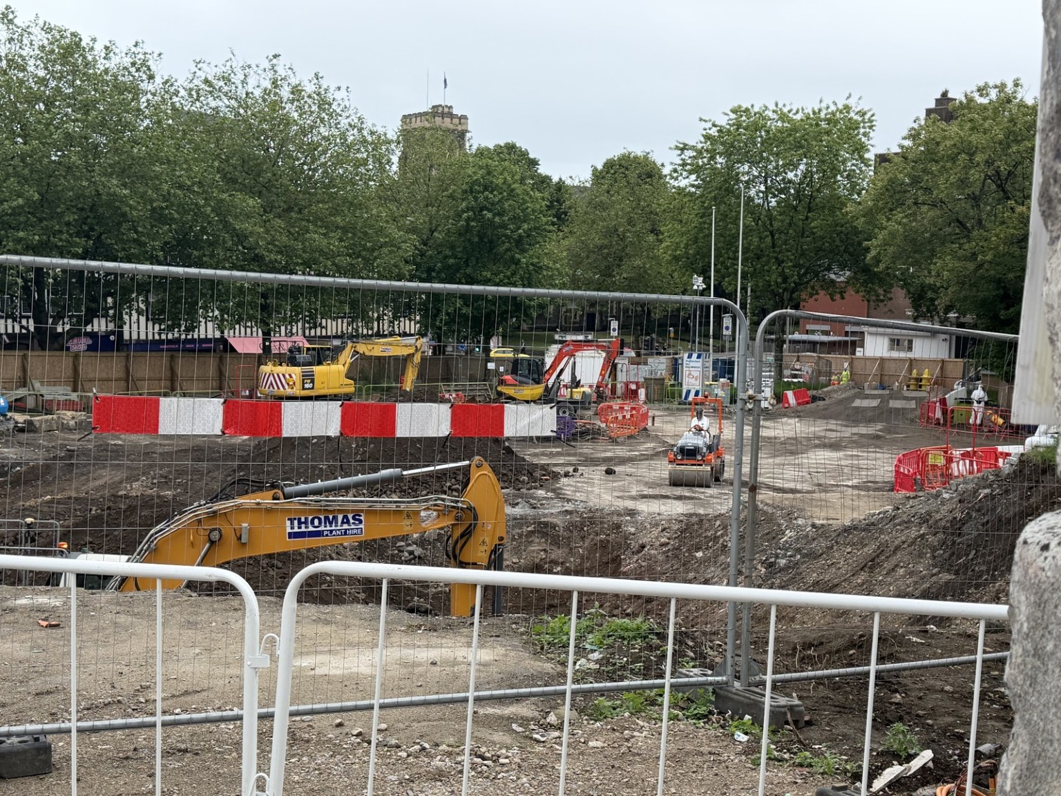Excavation work in Castle Square behind site fencing, with a Thomas Plant Hire digger and the ruins of Swansea Castle behind.