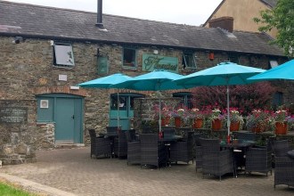 The stone exterior and outdoor terrace of Florentino’s Italian restaurant in Carmarthen, with teal parasols and flowers.