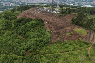 An aerial view of Kilvey Hill showing a large area of cleared ground and earthworks near the summit masts, with Swansea and the stadium in the distance.