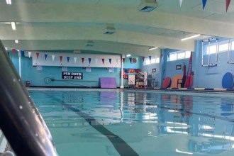 Inside Newcastle Emlyn's community swimming pool, with red, white and blue bunting and a bilingual 'Pen Dwfn / Deep End' sign.
