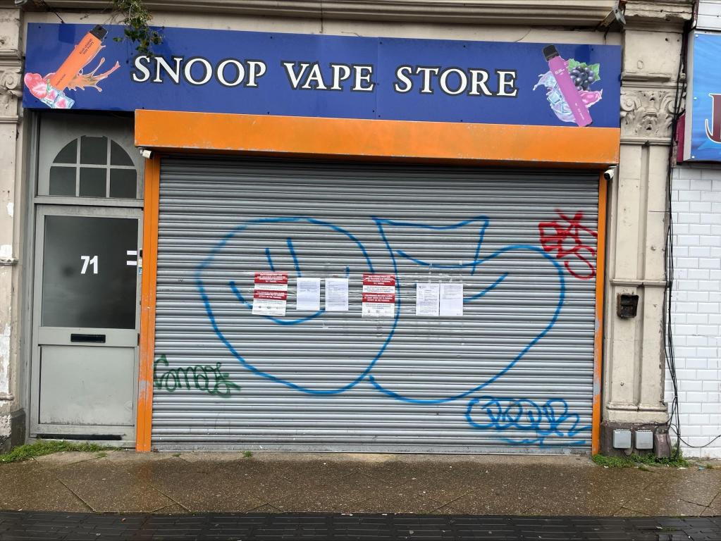 The closed orange-and-blue shutter of Snoop Vape Store on High Street, Swansea, with official Trading Standards closure notices taped to it.