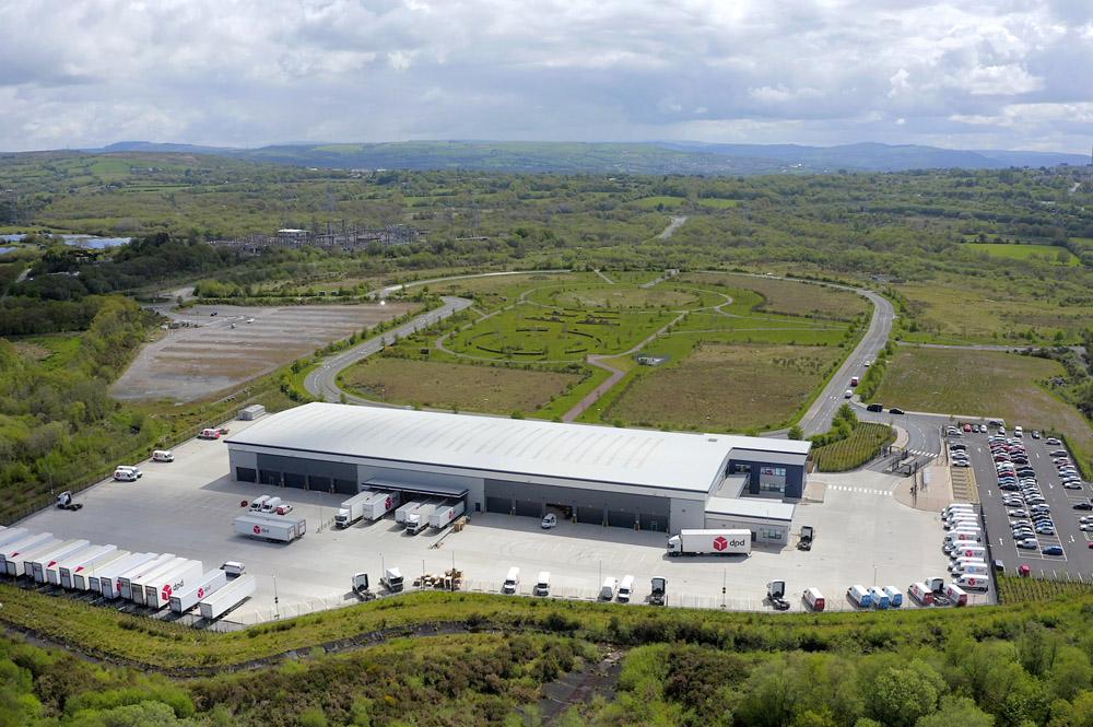 Aerial view of the DPD parcel distribution centre at Parc Felindre, its loading bays and parked delivery trailers in the foreground and undeveloped land behind.
