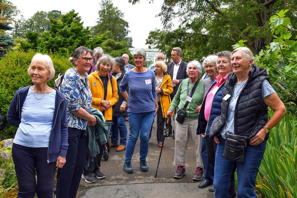 A large group of Friends of Swansea Botanical Gardens volunteers standing together on a path among the greenery.