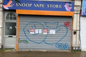 The closed orange-and-blue shutter of Snoop Vape Store on High Street, Swansea, with official Trading Standards closure notices taped to it.