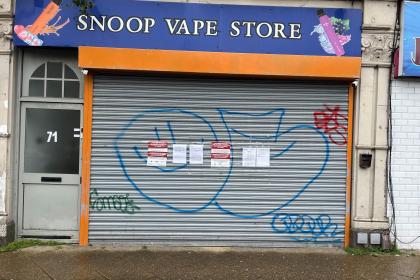 The closed orange-and-blue shutter of Snoop Vape Store on High Street, Swansea, with official Trading Standards closure notices taped to it.