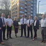 A group of eight people, including police officers in uniform and people in business dress, standing together outdoors in front of the Dyfatty flats.