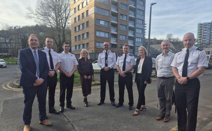 A group of eight people, including police officers in uniform and people in business dress, standing together outdoors in front of the Dyfatty flats.