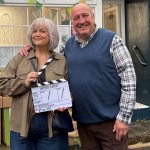 Ruth Jones and Steve Speirs smiling outside a village shop, Jones holding a clapperboard reading "Better Later", on the comedy's first day of filming.