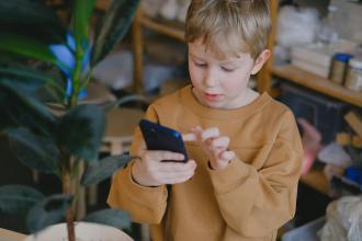 a boy wearing a brown sweater using a smartphone