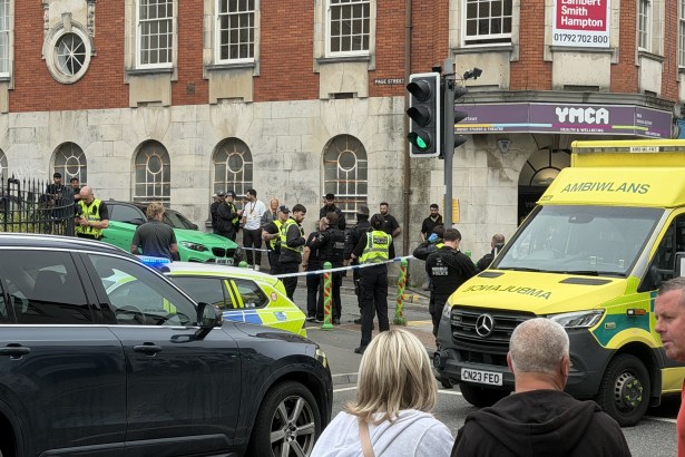 Police officers, some in armed-response gear, and a Welsh Ambulance Service crew behind a cordon on St Helen's Road near the YMCA in Swansea.