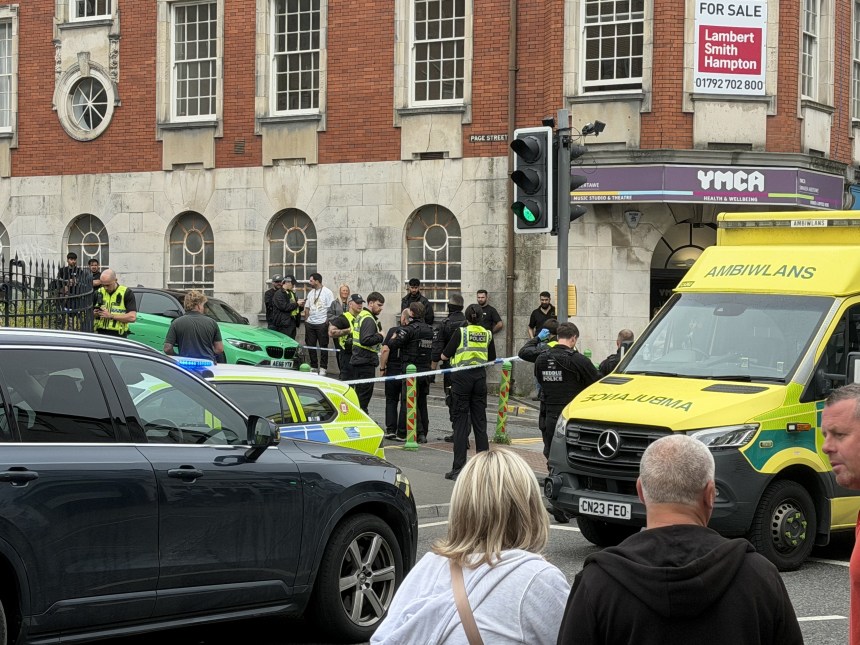 Police officers, some in armed-response gear, and a Welsh Ambulance Service crew behind a cordon on St Helen's Road near the YMCA in Swansea.