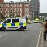 A South Wales Police van parked across St Helen's Road with emergency vehicles and onlookers further along the street.