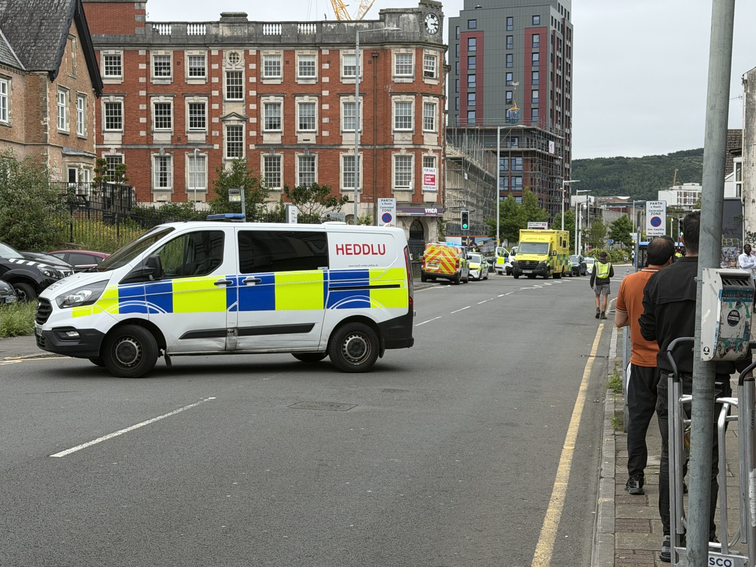 A South Wales Police van parked across St Helen's Road with emergency vehicles and onlookers further along the street.