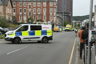 A South Wales Police van parked across St Helen's Road with emergency vehicles and onlookers further along the street.