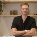 A vet in black scrubs stands with his arms folded in a clinic.