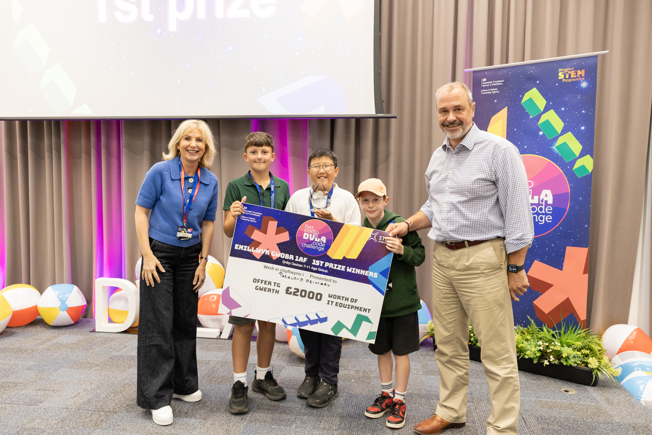 Three Parkland Primary pupils holding a giant first prize cheque, flanked by host Sian Lloyd and DVLA Chief Executive Tim Moss