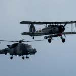 A WWII Fairey Swordfish biplane flying alongside a Westland Wasp helicopter over Swansea Bay