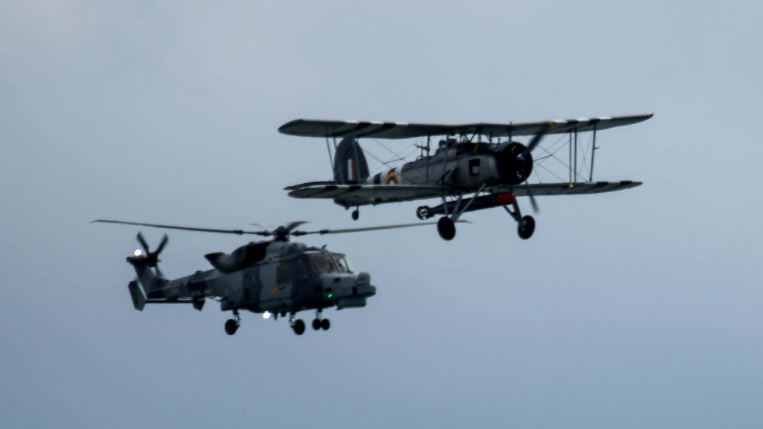 A WWII Fairey Swordfish biplane flying alongside a Westland Wasp helicopter over Swansea Bay