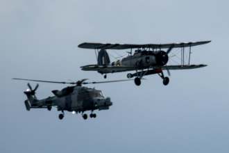 A WWII Fairey Swordfish biplane flying alongside a Westland Wasp helicopter over Swansea Bay
