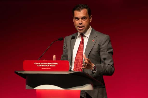Ken Skates in a grey suit and red tie speaking at a red Welsh Labour lectern reading Gyda'n Gilydd Dros Gymru — Together for Wales