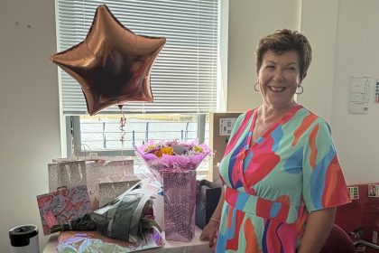 Tracy Pike MBE smiling beside flowers, gifts and a balloon at her retirement celebration