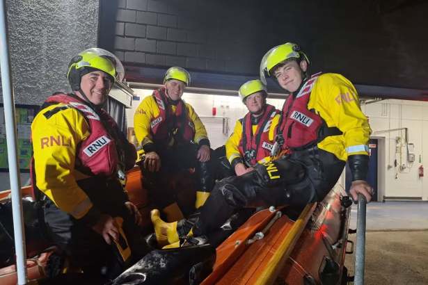 Four RNLI lifeboat crew in yellow and red kit and helmets sitting on their lifeboat inside the Horton and Port Eynon station