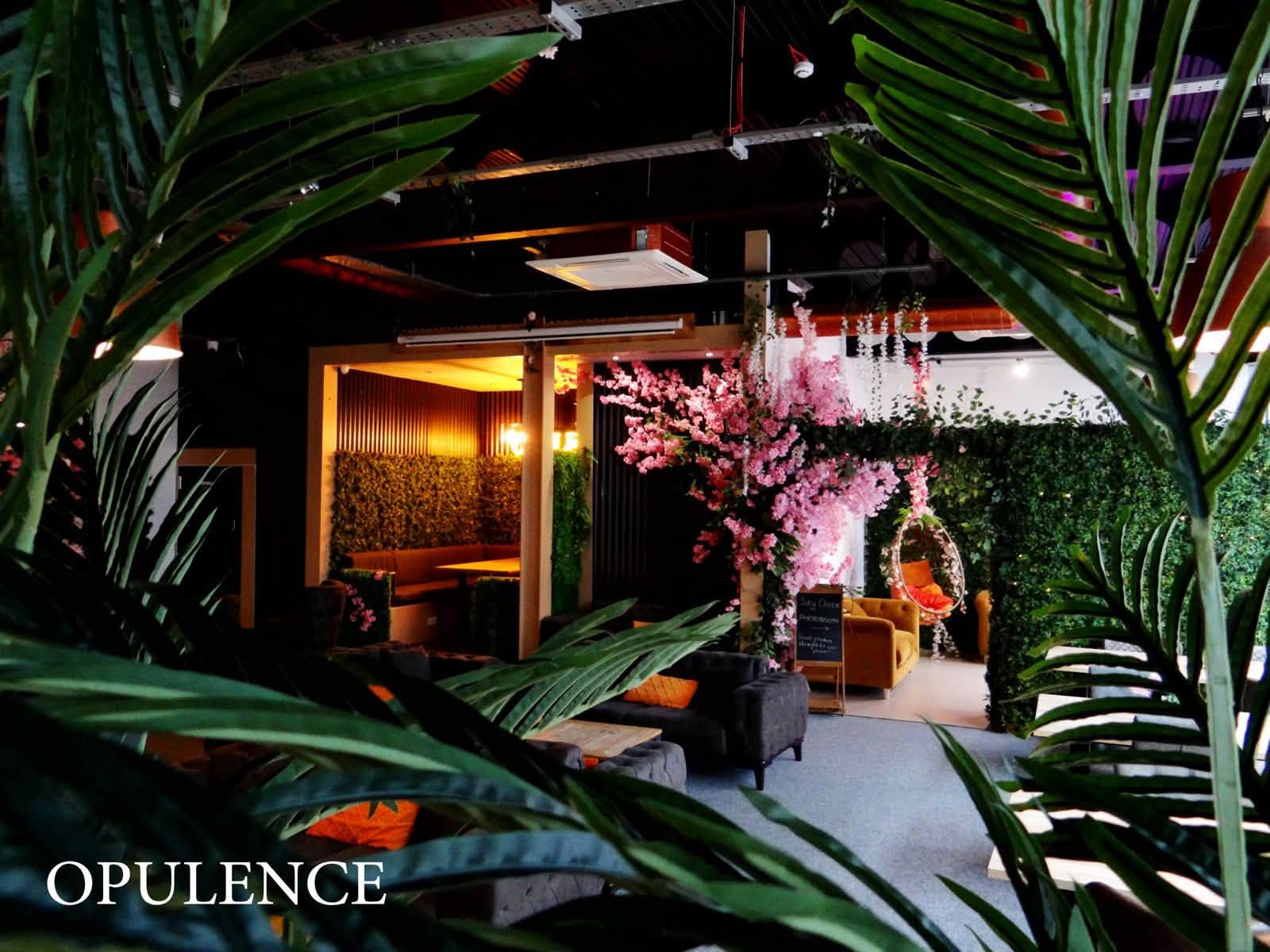 A lounge area at Opulence with pink blossom, hanging egg chair and foliage walls
