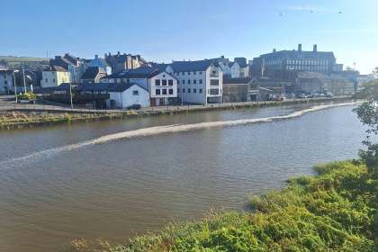 A line of foam stretching along the River Towy at Carmarthen, with the town's riverside buildings in the background
