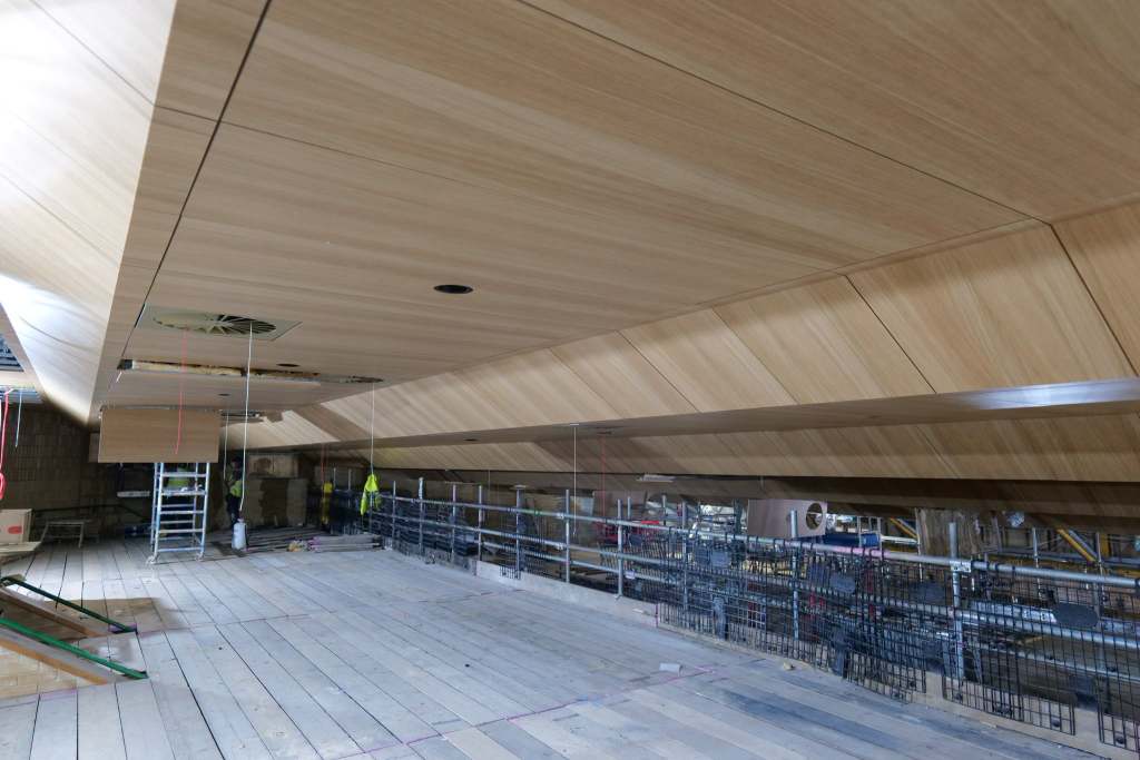 The new angled oak-panelled ceiling installed above the balcony level of the Princess Royal Theatre auditorium, with scaffolding on the construction site below