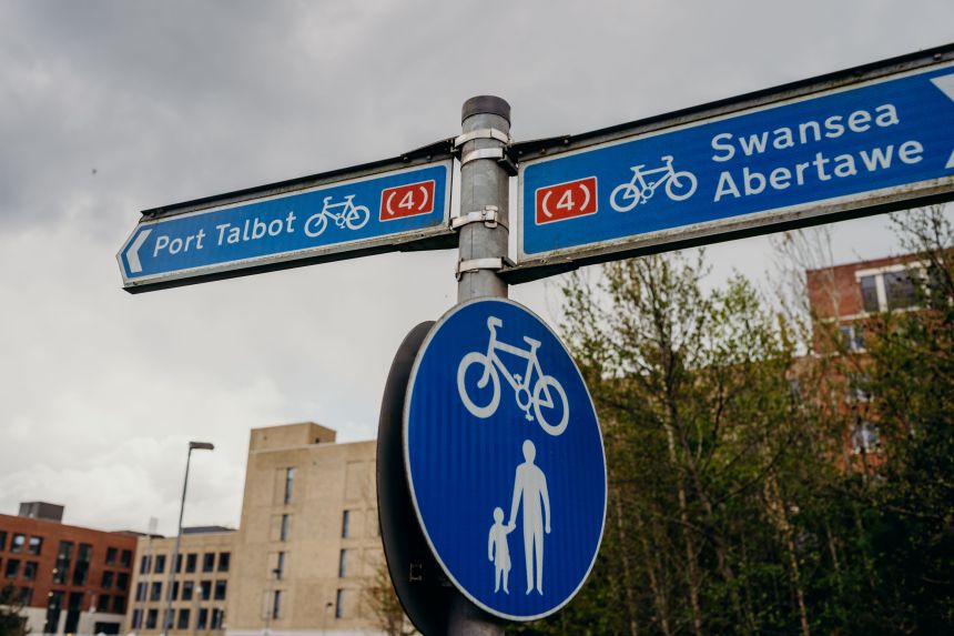 A blue cycle route signpost showing directions to Swansea and Port Talbot along National Cycle Network Route 4, with a shared-use path sign below.