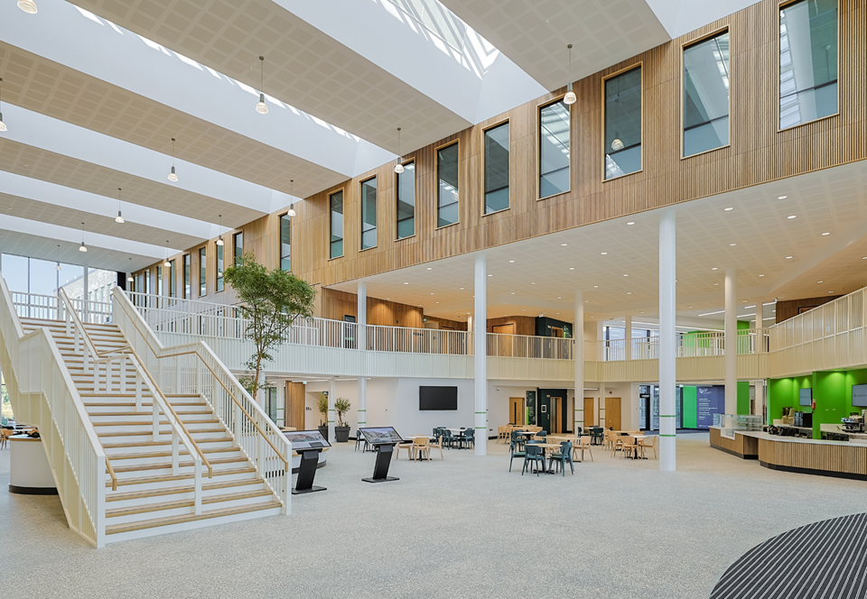 The bright timber-lined atrium inside Canolfan Pentre Awel with a white staircase, cafe seating and skylights