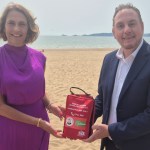 Melanie James and Cllr Rob Stewart holding a red public access bleed control kit on the beach at Swansea Bay