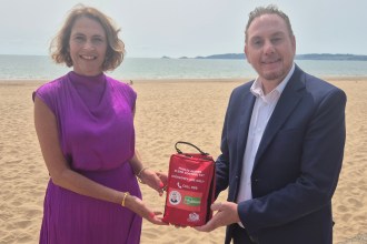 Melanie James and Cllr Rob Stewart holding a red public access bleed control kit on the beach at Swansea Bay