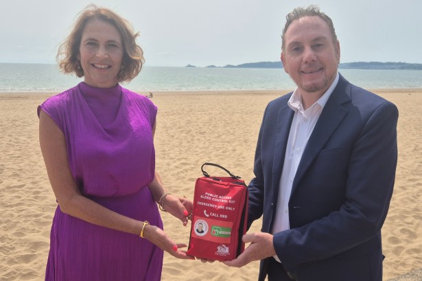Melanie James and Cllr Rob Stewart holding a red public access bleed control kit on the beach at Swansea Bay