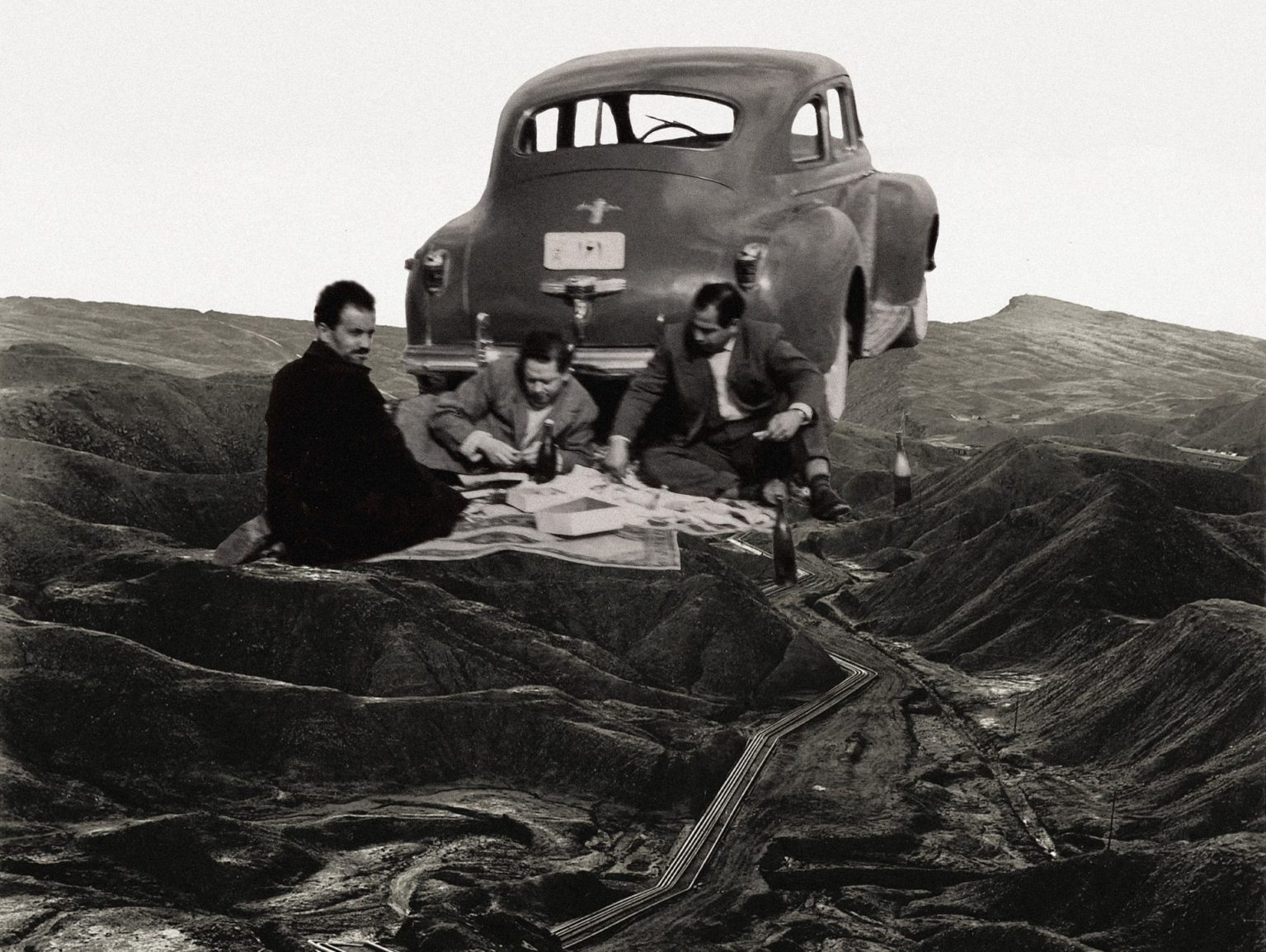 A black and white collage of three men picnicking beside a vintage car on a barren hilly landscape crossed by oil pipelines.