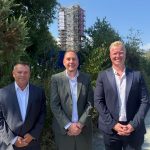 David James, Rob Stewart and Ross Miller standing in front of greenery at the Hafod-Morfa Copperworks, with the scaffolded engine house tower behind them