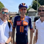 Two men in Cycle Champs polo shirts standing either side of a professional cyclist in Picnic PostNL kit at the Tour de France
