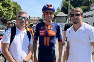 Two men in Cycle Champs polo shirts standing either side of a professional cyclist in Picnic PostNL kit at the Tour de France