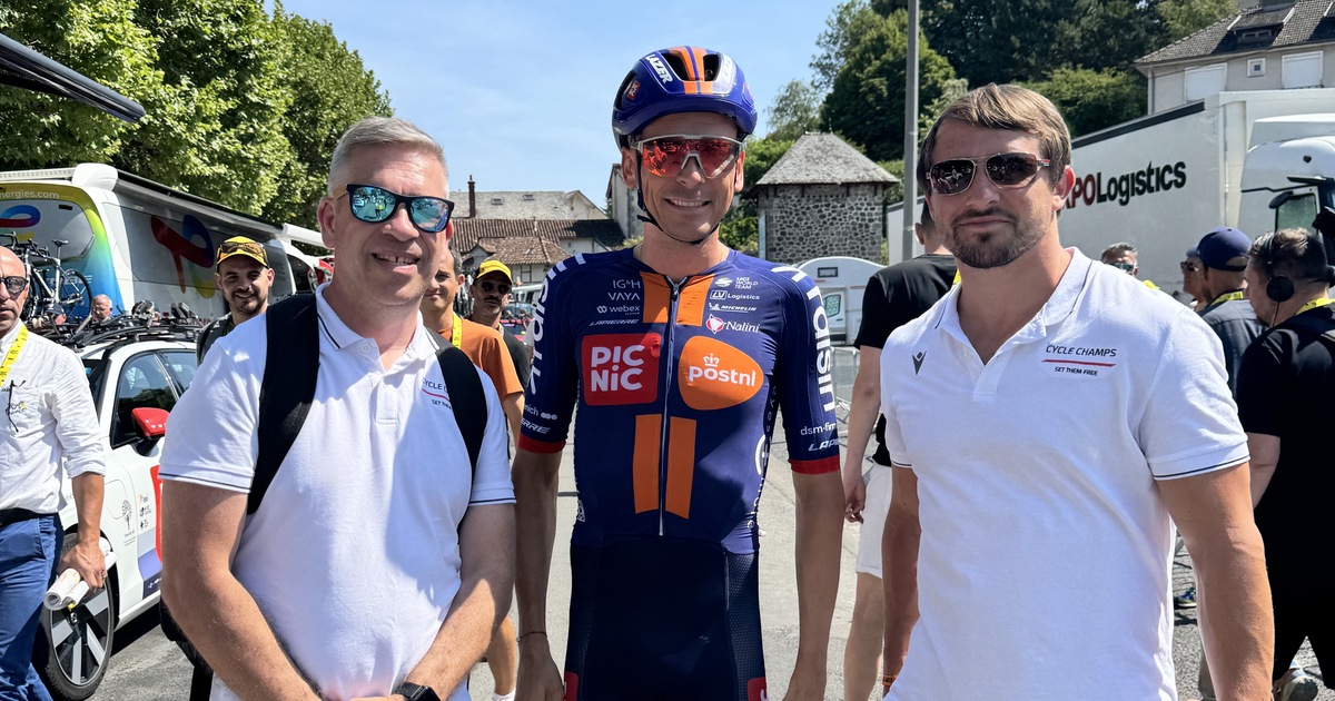 Two men in Cycle Champs polo shirts standing either side of a professional cyclist in Picnic PostNL kit at the Tour de France