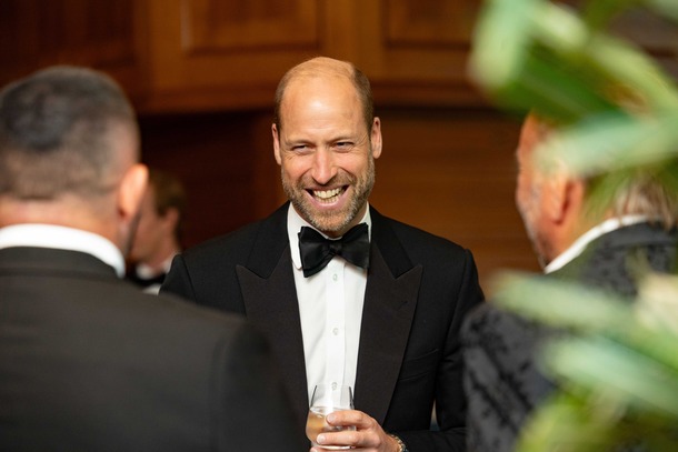  The Prince of Wales smiling in a black dinner jacket and bow tie while talking with guests.