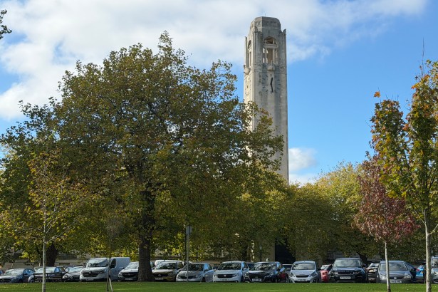 The clock tower of Swansea's Guildhall rising above trees, with cars parked in front of the building