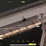 Aerial police camera view of a rider on an electric motorbike crossing a pedestrian footbridge over water